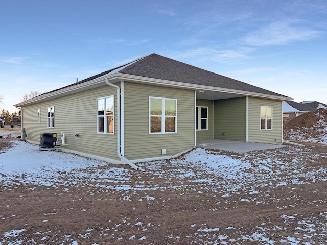 snow covered back of property with central AC unit and a patio