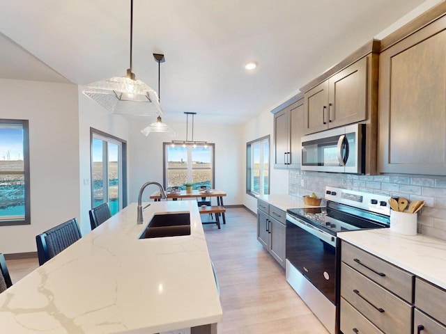 kitchen featuring pendant lighting, stainless steel appliances, an island with sink, decorative backsplash, and light stone counters