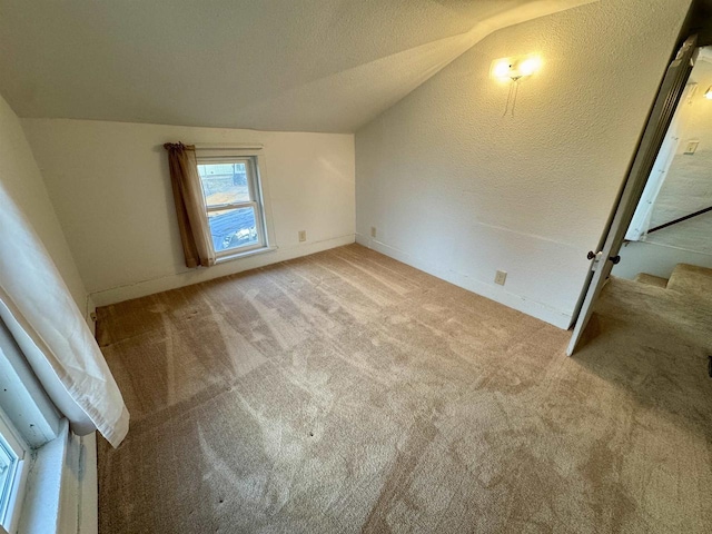 bonus room featuring vaulted ceiling, a textured ceiling, and light colored carpet