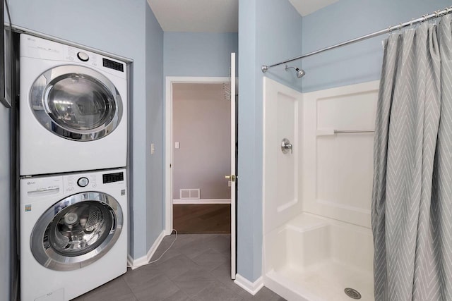 washroom with stacked washer / drying machine and dark tile patterned flooring