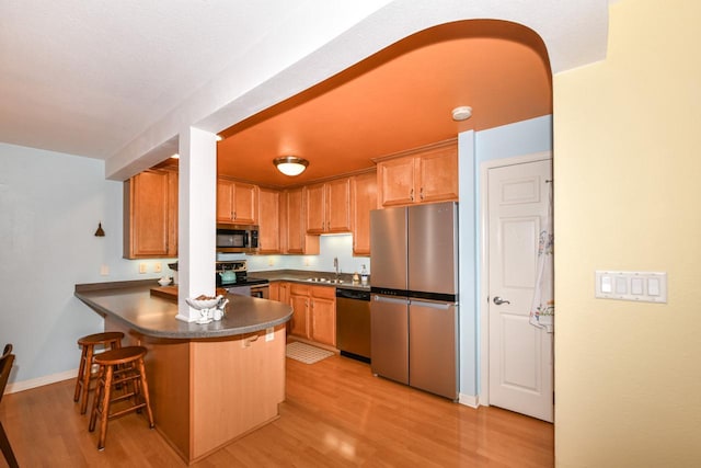 kitchen featuring kitchen peninsula, sink, light wood-type flooring, appliances with stainless steel finishes, and a kitchen breakfast bar