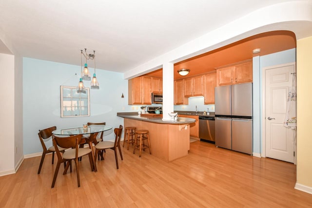 kitchen featuring pendant lighting, appliances with stainless steel finishes, a kitchen bar, kitchen peninsula, and light wood-type flooring