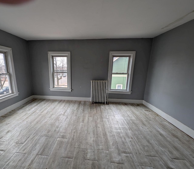 spare room with radiator heating unit, a healthy amount of sunlight, and light hardwood / wood-style floors