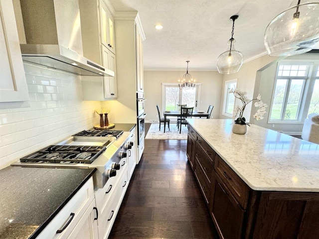 kitchen featuring white cabinets, appliances with stainless steel finishes, wall chimney exhaust hood, and dark stone countertops