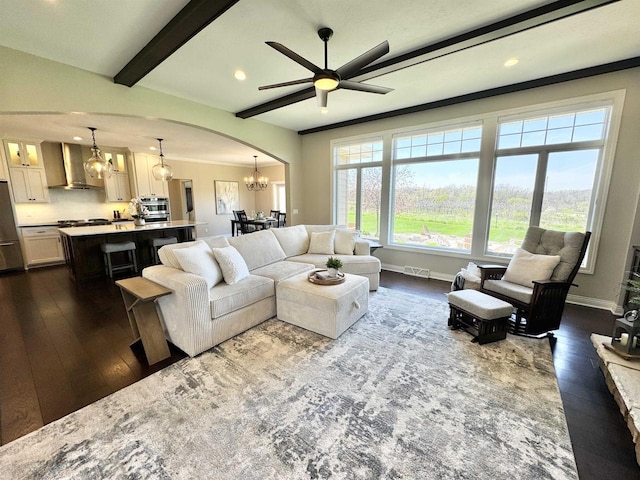 living room with ceiling fan with notable chandelier, dark wood-type flooring, and beam ceiling