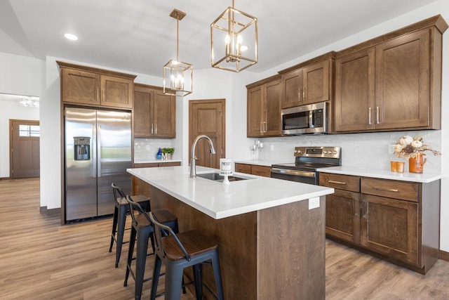 kitchen with appliances with stainless steel finishes, decorative light fixtures, sink, a kitchen island with sink, and decorative backsplash