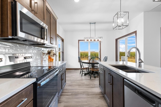 kitchen featuring appliances with stainless steel finishes, dark brown cabinetry, decorative light fixtures, sink, and backsplash