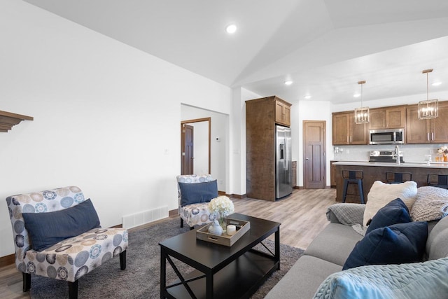 living room with sink, light wood-type flooring, and lofted ceiling