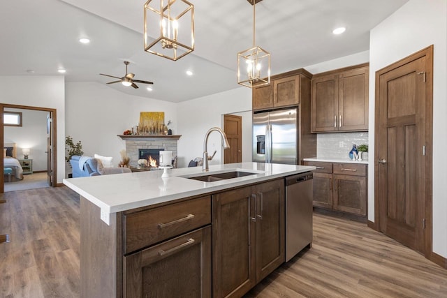 kitchen with appliances with stainless steel finishes, a stone fireplace, sink, backsplash, and a center island with sink