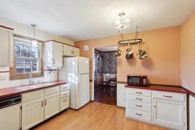 kitchen featuring decorative backsplash, white appliances, light wood-type flooring, pendant lighting, and sink