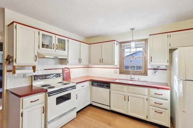 kitchen with pendant lighting, white appliances, white cabinetry, sink, and light wood-type flooring