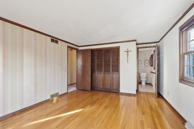 unfurnished bedroom with ensuite bathroom, a closet, crown molding, and light wood-type flooring