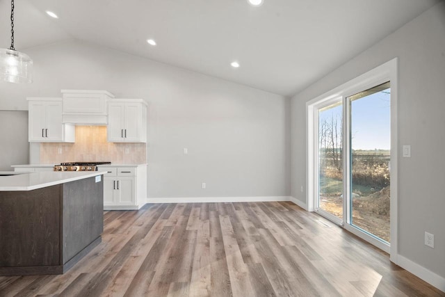 kitchen with white cabinets, decorative backsplash, light hardwood / wood-style floors, hanging light fixtures, and vaulted ceiling