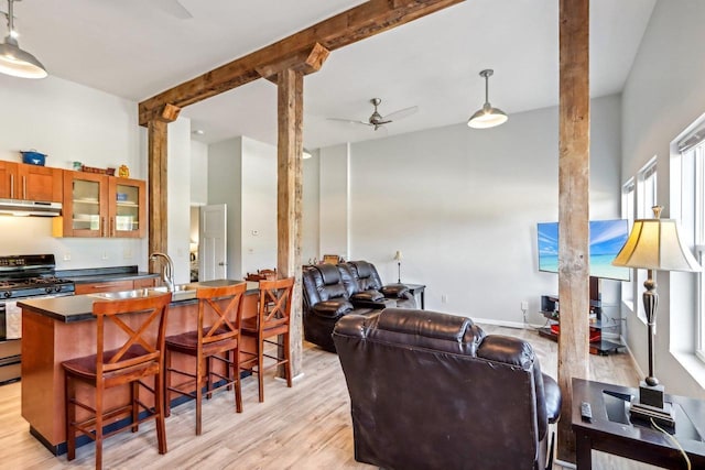 kitchen featuring sink, stainless steel range with gas stovetop, hanging light fixtures, light wood-type flooring, and a kitchen breakfast bar