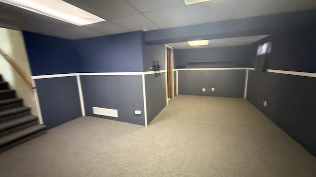 basement featuring a paneled ceiling and light colored carpet