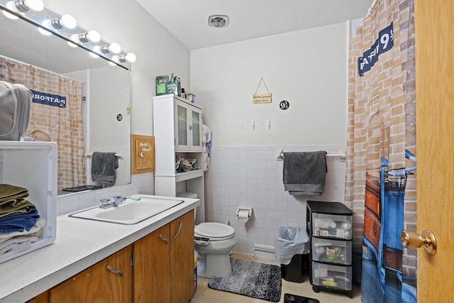 bathroom featuring vanity, toilet, tile walls, and a baseboard heating unit