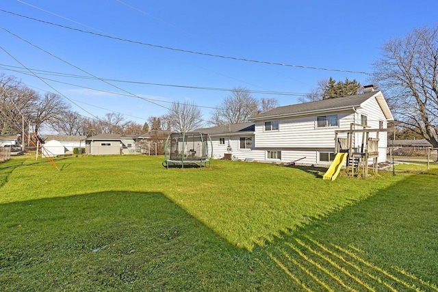 back of property featuring a trampoline, a playground, and a lawn