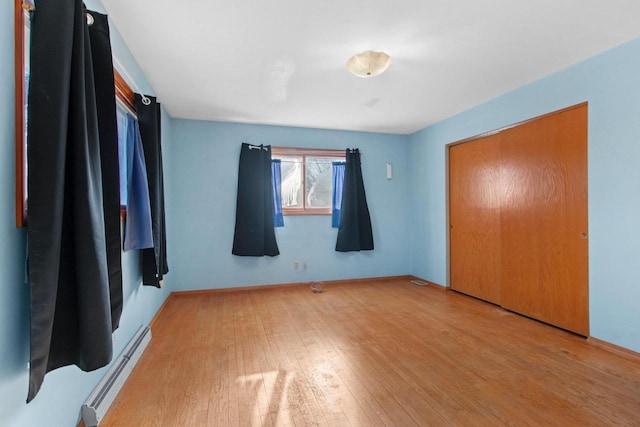 unfurnished bedroom featuring a closet, a baseboard radiator, and wood-type flooring