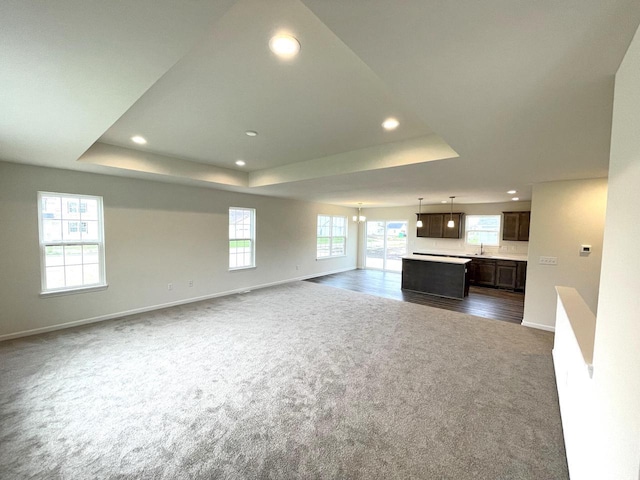 unfurnished living room featuring sink, a raised ceiling, and dark colored carpet