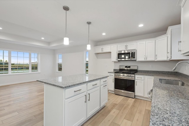 kitchen with light stone countertops, appliances with stainless steel finishes, white cabinetry, sink, and a kitchen island