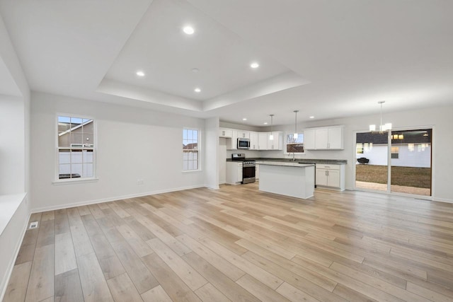 kitchen with a center island, appliances with stainless steel finishes, white cabinetry, hanging light fixtures, and a tray ceiling