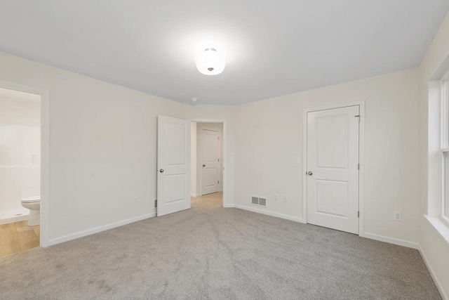 unfurnished bedroom featuring connected bathroom and light colored carpet