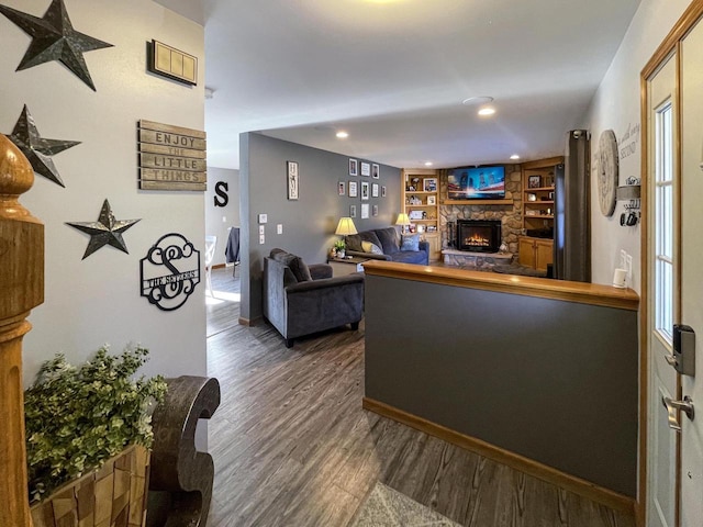 living room with built in shelves, dark hardwood / wood-style floors, and a stone fireplace