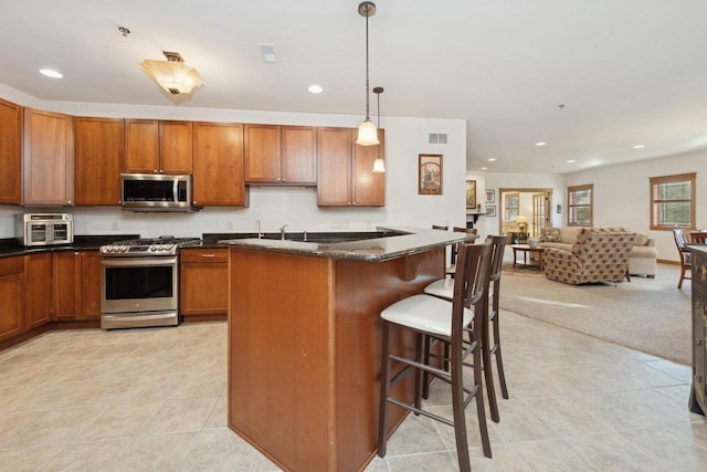 kitchen with appliances with stainless steel finishes, dark stone countertops, a kitchen island, pendant lighting, and a breakfast bar