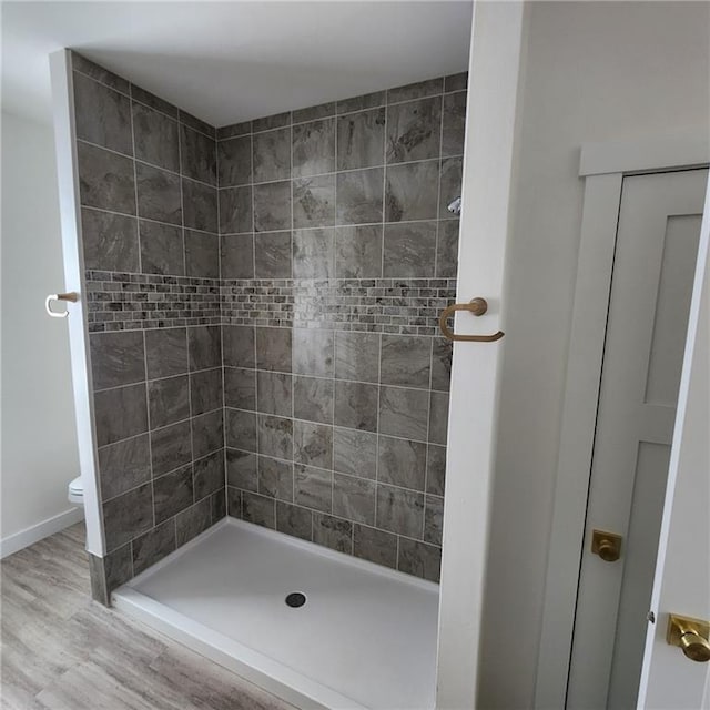 bathroom featuring wood-type flooring, toilet, and a tile shower