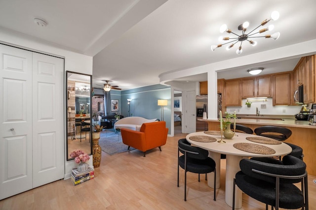 dining area with ceiling fan with notable chandelier and light hardwood / wood-style floors