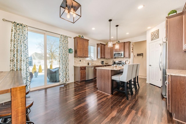 kitchen with appliances with stainless steel finishes, decorative light fixtures, light stone counters, dark hardwood / wood-style floors, and a kitchen island