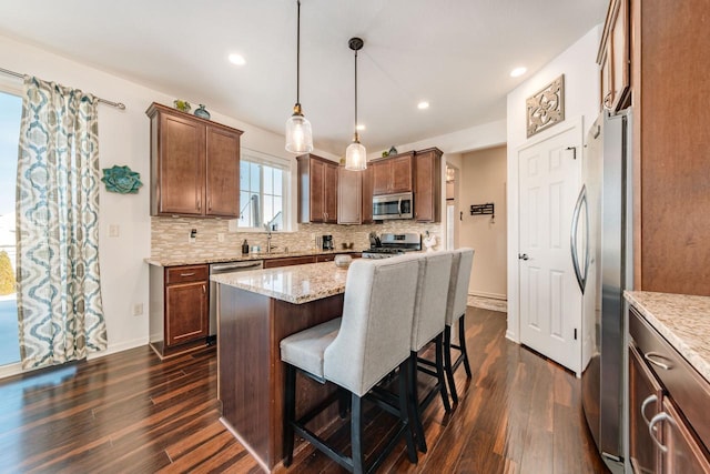 kitchen featuring tasteful backsplash, hanging light fixtures, a kitchen island, stainless steel appliances, and light stone counters