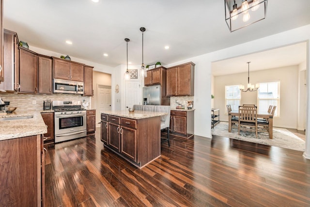 kitchen featuring light stone countertops, appliances with stainless steel finishes, a kitchen island, decorative light fixtures, and backsplash