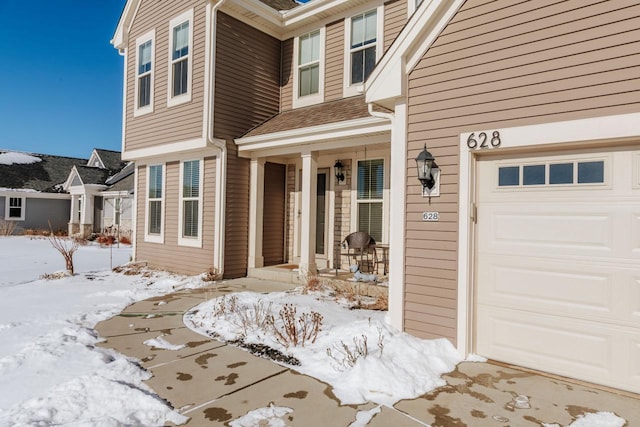 snow covered property entrance featuring a garage and a porch