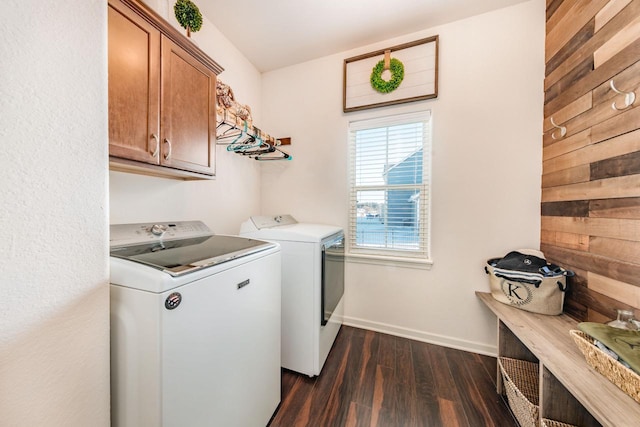 clothes washing area with washing machine and dryer, wood walls, dark hardwood / wood-style floors, and cabinets