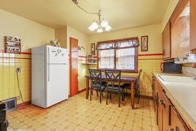 kitchen with pendant lighting, white refrigerator, sink, tile walls, and a notable chandelier