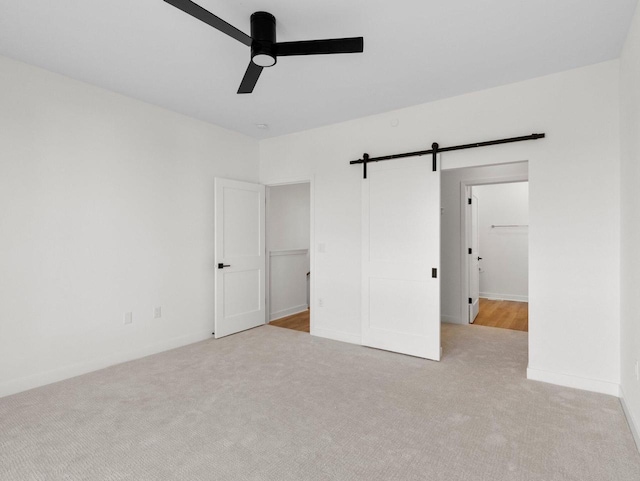 unfurnished bedroom with light carpet, ensuite bath, ceiling fan, and a barn door