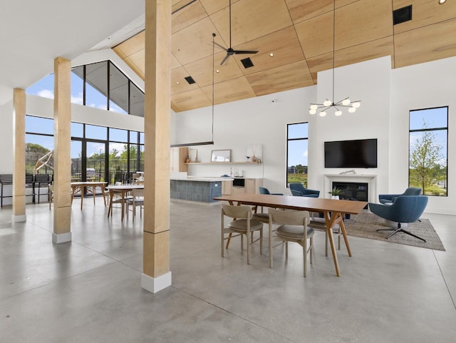 dining space with a healthy amount of sunlight, ceiling fan with notable chandelier, concrete flooring, and a high ceiling