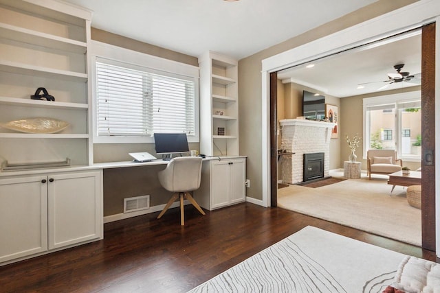 home office with dark hardwood / wood-style flooring, a brick fireplace, a wealth of natural light, and built in features