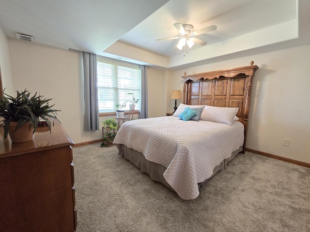 carpeted bedroom featuring ceiling fan and a tray ceiling