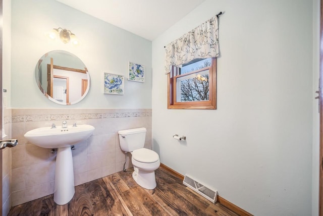 bathroom with toilet, hardwood / wood-style floors, and tile walls