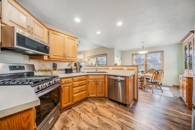 kitchen with pendant lighting, light hardwood / wood-style flooring, appliances with stainless steel finishes, sink, and backsplash