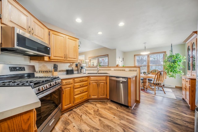 kitchen featuring appliances with stainless steel finishes, decorative light fixtures, wood-type flooring, tasteful backsplash, and sink