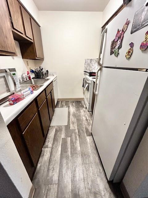 kitchen with sink, dark brown cabinets, white appliances, and light hardwood / wood-style flooring