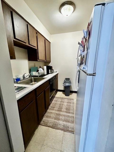 kitchen with dark brown cabinetry, white fridge, sink, wall oven, and light tile patterned flooring