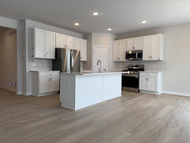 kitchen with white cabinetry, stainless steel appliances, and an island with sink