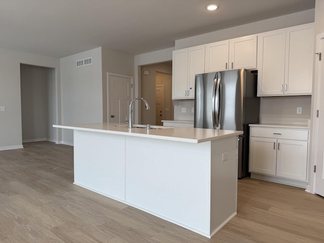 kitchen with sink, a center island with sink, white cabinets, and stainless steel refrigerator