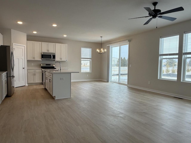 kitchen with appliances with stainless steel finishes, white cabinetry, an island with sink, hanging light fixtures, and light wood-type flooring