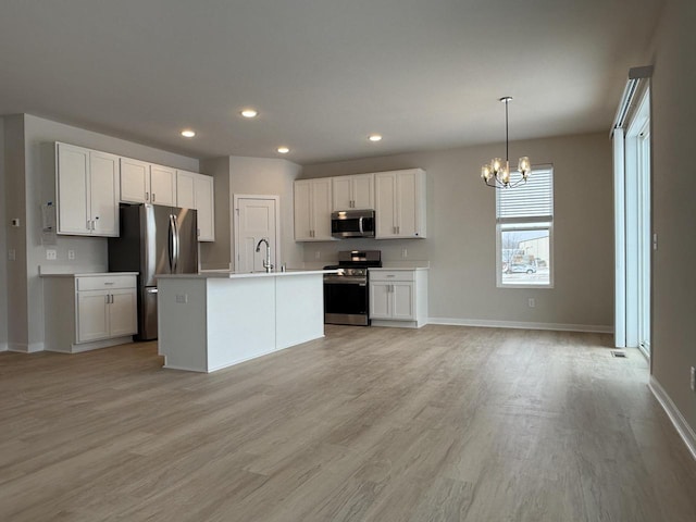 kitchen featuring hanging light fixtures, white cabinets, sink, an island with sink, and stainless steel appliances