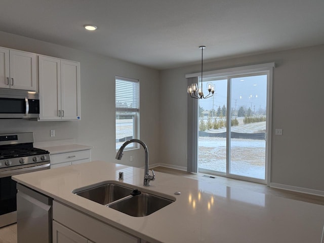 kitchen featuring pendant lighting, white cabinetry, stainless steel appliances, sink, and a notable chandelier